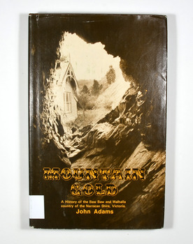 Hardback. Brown dust cover. Photograph on front cover looks out from the entry of a mine onto the front of a building which has a hill to the side of it. The back cover has a photograph of the side of a hill with some trees on it.