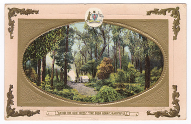 Printed postcard showing a coloured photograph of a small hut in the bush land at Marysville, Victoria. The oval shaped photograph is surrounded by a gold printed frame, the Australian coat of arms is centered at top. On the reverse is a handwritten message written in black ink. There is a space to place a postage stamp.