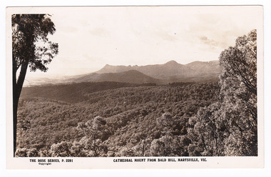 Shows a view of the range of mountains known as the Cathedral Range including Mount Cathedral. In the foreground are a series of heavily forested hills. On the reverse of the postcard is space to write a message and an address and to place a postage stamp. The postcard is unused.