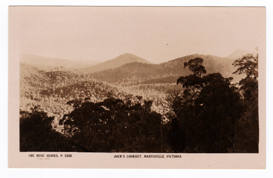 An early sepia photograph of the view of the surrounding mountains taken from Jock's Lookout which is on the Marysville-Wood's Point Road near Marysville in Victoria. Shows heavily forested mountains in the background. On the reverse of the postcard is a space to write a message and an address and to place a postage stamp. The postcard is unused.