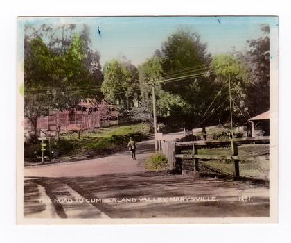Shows the intersection of the Buxton Marysville Road and the Marysville-Wood's Point Road. In the right of the photograph The Crossways Hotel can just be seen. In the background can be seen the Marysville Chalet Guest House. There is a man standing in the middle of the Marysville-Wood's Point Road. The title of the photograph is handwritten in white ink along the lower edge.