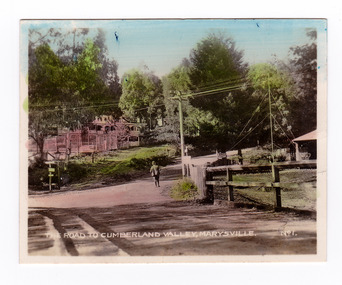 Shows the intersection of the Buxton Marysville Road and the Marysville-Wood's Point Road. In the right of the photograph The Crossways Hotel can just be seen. In the background can be seen the Marysville Chalet Guest House. There is a man standing in the middle of the Marysville-Wood's Point Road. The title of the photograph is handwritten in white ink along the lower edge.