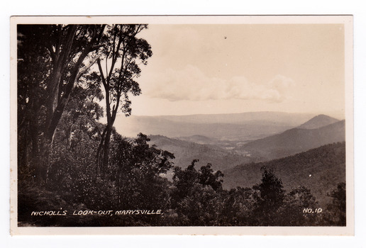 Shows the view from Nicholl's Look-out near Marysville in Victoria. Shows a view of mountains with trees in the foreground. The title of the photograph is handwritten in white ink on the lower edge.