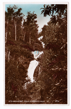 Shows Steavenson Falls in Marysville, Victoria. Shows the three cascades flowing down a mountain. The falls are surrounded by a forest of trees. The title of the photograph is handwritten in white ink on the lower edge. On the reverse is a space to write a message and to place a postage stamp.