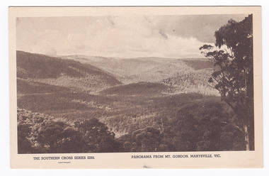 Shows the view from Mount Gordon over the mountains surrounding Marysville in Victoria. In the foreground are some trees. In the background can be seen a series of heavily forested mountains. On the reverse of the postcard is a space to write a message and an address and to place a postage stamp. The postcard is unused.