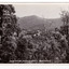 Shows the view from Jock's Lookout of Marysville in Victoria. In the distance can be seen various buildings in Marysville. In the foreground are several trees and in the background are heavily forested mountains. The title of the photograph is handwritten in white ink on the lower edge. On the reverse of the postcard is space to write a message and an address and to place a postage stamp. The postcard is unused.