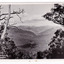 Shows the view of Marysville taken from Mount Gordon. In the distance can be seen the buildings of Marysville surrounded by heavily forested mountains. In the foreground are some large trees. The title of the photograph is handwritten in white ink on the lower edge. On the reverse there is a handwritten message.
