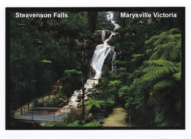 Shows Steavenson Falls in Marysville in Victoria. The photograph shows the footbridge over the falls that was built after the Black Saturday bushfires which destroyed Marysville and the surrounding area. On the reverse of the postcard is a space to write a message and an address and to place a postage stamp. The postcard is unused.