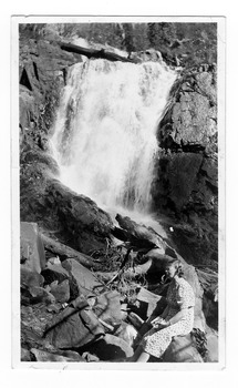 An early black and white photograph of Steavenson Falls in Marysville in Victoria. In the photograph there is a lady sitting on rocks at the base of the falls. On the reverse of the photograph the location of the photograph is handwritten in black ink.