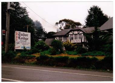 Shows Tudor Lodge Roadhouse in Narbethong in Victoria. Shows a large tudor style building surrounded by trees and hedges. Shows a large sign out the front advertising the lodge, a roadhouse and cafe and discount ski hire.