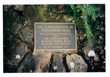 Shows a sign that is at Steavenson Falls in Marysville in Victoria. Shows details of when the floodlights were first switched on at the falls in November, 1972. The sign is metal and is set into a stone at the falls.