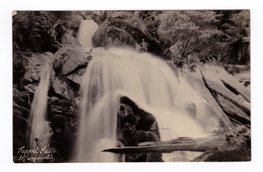 Shows Keppel Falls near Marysville in Victoria. In the middle of the photograph, near the top edge of the postcard, there is a man standing on rocks above the falls. The title of the postcard is handwritten in white ink on the lower-left edge. On the reverse of the postcard is a space to write a message and an address and to place a postage stamp. The postcard is unused.