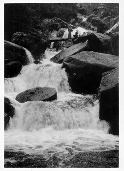 Shows a group of three ladies standing on a wooden log bridge that lays across Keppe Falls near Marysville in Victoria.