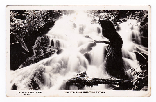 Shows the Cora Lynn Falls which are in Cambarville. Shows the falls cascading over rocks. There are a number of fallen logs lying across the falls. On the reverse is a space to write a message and an address and to place a postage stamp. The postcard is unused.