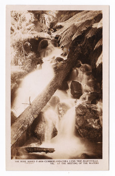 Shows the Cora-Lynn waterfalls at the Meeting of the Waters near Cumberland Creek. Shows the waterfall cascading down the mountain. In the foreground there is a fallen log lying across the falls. In the background are some tree ferns. On the reverse of the postcard is space to write a message and an address and place a postage stamp. The postcard is unused.