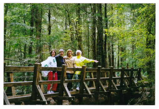 Shows 4 ladies standing a wooden bridge that leads to The Big Tree near Cambarville in Victoria.