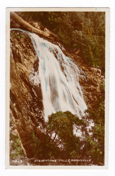 Shows Steavenson Falls in Marysville in Victoria. Shows the falls cascading down the mountain surrounded by forest. The title of the photograph is handwritten in white ink along the lower edge.