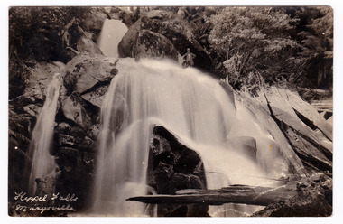 Shows Keppel Falls near Marysville in Victoria. In the middle of the photograph, near the top edge of the postcard, there is a man standing on rocks above the falls. The title of the postcard is handwritten in white ink in the lower left corner. On the reverse of the postcard is a space to write a message and an address and to place a postage stamp. The postcard is unused.