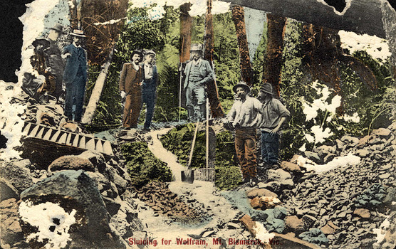 Shows a group of five men standing with various shovels next to a sluice box which is sitting on top of some rocks at the Wilks Creek wolfram mine near Marysville in Victoria. Sitting at the foot of one of the men is a gold mining pan. The men are standing in a forest. The title of the photograh is written in red along the lower edge of the photograph.