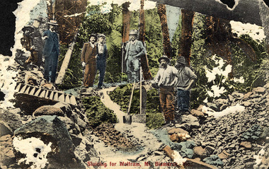 Shows a group of five men standing with various shovels next to a sluice box which is sitting on top of some rocks at the Wilks Creek wolfram mine near Marysville in Victoria. Sitting at the foot of one of the men is a gold mining pan. The men are standing in a forest. The title of the photograh is written in red along the lower edge of the photograph.
