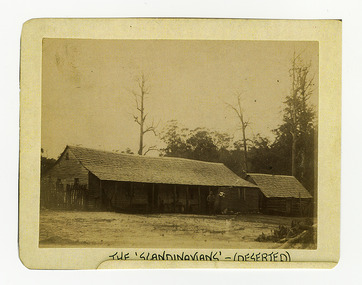 Shows the rear view of The Scandinavians' which was a hotel and boarding house along the Yarra Track. Shows a timber clad building with a timber shingled roof. At the right of the building is a wooden picket fence and at the left of the building is another timber clad building. Under the verandah of the main building can be seen various items. There is a man standing in front of the building. The title of the photograph is along the lower edge in black ink. On the reverse of the photograph is a stamp from the Armstrong Collection at 42 Station Street in Sandringham in Victoria.