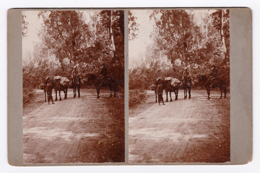 Shows a group of three men, two mounted and one standing with three saddled horses and one pack horse. They are standing on a dirt road. The subject and photograph location are written on the reverse in black lead pencil.