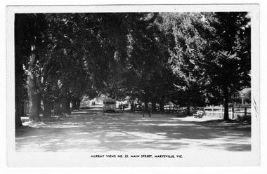 Shows Murchison Street in Marysville in Victoria. Shows a tree lined street with several people walking along it. In the left of the photograph can be seen the rear of a caravan. On the right can be seen a wooden bench seat and further down there is a parked car. There is a bus travelling along the road as well. The title of the photograph is along the lower edge of the photograph.