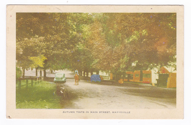 Show Murchison Street in Marysville in Victoria during Autumn. Shows a tree lined street with a car parked on both sides of the street. There is a woman on a horse riding up the middle of the street. On the right hand side are several shops. The title of the photograph is along the lower edge of the postcard. On the reverse of the postcard is a handwritten message in lead pencil.