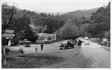 Shows Murchison Street in Marysville in Victoria in April 1949. In the left of the photograph is The Australian Hotel with The Cumberland Guest House further down the road. There are several vehicles of various types parked and travelling along the road alongside two people on horseback. There are also a number of pedistrians standing or walking along both sides of the road. In the background is forest and mountains can be seen in the distance. The subject and date the photograph was taken are on the reverse.