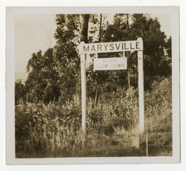 Shows the 'Marysville' sign on Murchison Street in Marysville in Victoria. Underneath 'Marysville' is a sign saying 'Please Slow Down'.