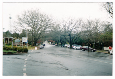 Shows Murchison Street in Marysville in Victoria. Shows the view looking up Murchison Street towards the corner with Lyell Street. The photograph was taken at the corner with Pack Road. In the foreground can be seen tourist signs to two attractions and a signpost showing various distances and locations. The photograph appears to have been taken after rain.