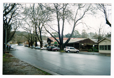 Shows Murchison Street in Marysville in Victoria. Shows the view looking up the right side of Murchison Street towards the corner with Pack Road. Shows buildings with various vehicles parked outside them. The photograph appears to have been taken after rain.