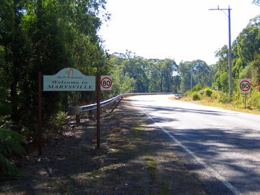 Shows Murchison Street in Marysville in Victoria. Shows the 'Mist Of The Mountains', 'Welcome to MARYSVILLE' sign that used to welcome visitors to Marysville with a speed limit of 80 sign attached.