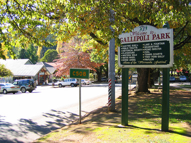 Shows the view looking down Murchison Street in Marysville in Victoria. In the foreground is the sign at the entrance to Gallipoli Park showing all the various amenities available for public use. On the opposite side of the road are various buildings with cars parked outside them.