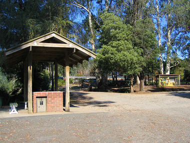 Shows the barbecue area that is situated behind the Visitor Information Centre in Marysville in Victoria. In the background can be seen a stationery engine that was in use at the Sund's sawmill which was previously located in Marysville.
