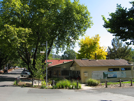Shows the view looking up Murchison Street in Marysville in Victoria. On the corner can be seen The Corner Cupboard Cafe. There is another building next to the cafe and there are cars parked along both sides of the street. Along the outside wall of the cafe are two large maps and a painting of Steavenson Falls.