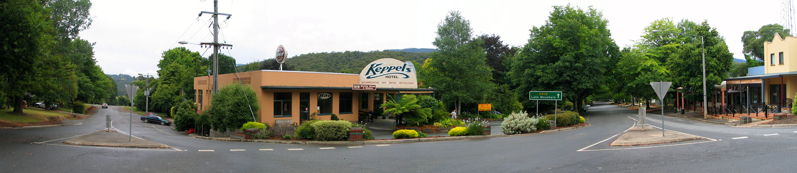 Shows Keppels Hotel on the corner of Murchison and Lyell Streets in Marysville in Victoria. View is looking down Murchison Street and down Lyell Street. On the opposite corner is a group of shops. In front of the hotel is a green sign showing the direction to drive to Lake Mountain.