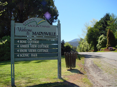 Shows a sign welcoming visitors to Marysville in Victoria. Shows the direction to travel to four different accommodation sites.