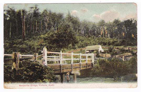 Shows a wooden, white painted bridge that crosses over a river. In the foreground, standing on the bank of the river, is a young girl wearing a hat. In the background is a timber building surrounded by wooden fences. Birthday Greetings have been written in glitter across the image. On the reverse of the postcard is a message and an address handwritten in black ink. There is also stamp affixed to the reverse alongside a date stamp.