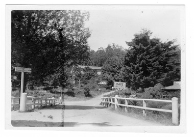 Shows a bridge that crosses over the Steavenson River in Marysville in Victoria. In the foreground on the bridge is a sign that directs visitors to the Michaeldene Track and to the Wishing Well. In the right of the photograph is The Crossways Hotel and in the background is Marysville Chalet.