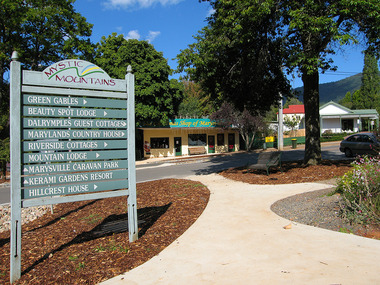 Shows a wooden information sign with the directions to various accommodation sites in Marysville in Victoria. In the background is the Marysville Christmas Shop.