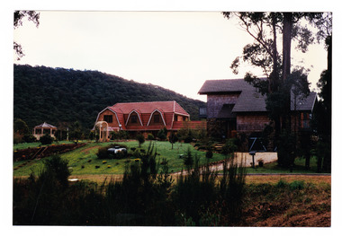 Shows two houses, both set in gardens with lawn and trees. One house is a timber clad two storey residence and the other is a Dutch gable style residence. Next to the Dutch gable house is a small gazebo.