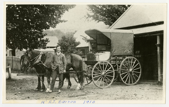 Shows a man standing next to a wagon advertising Barton Bros Store. The wagon is being pulled by two horses. In the background can be seen three buildings. The name of the man and the year the photograph was taken has been hand written along the lower edge.