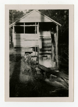 Shows a wooden building which houses a water wheel.