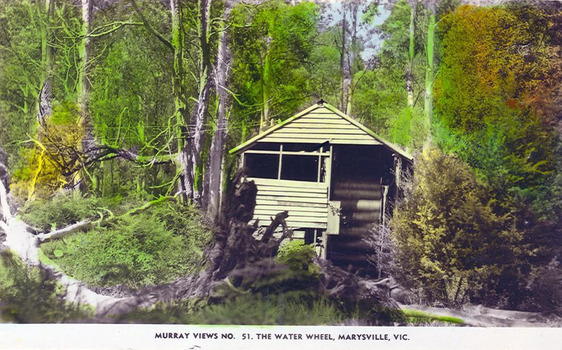 Shows a wooden building which houses a water wheel.