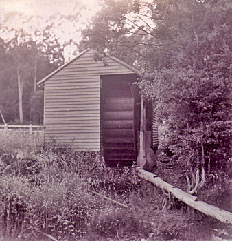 Shows a wooden building which houses a water wheel.