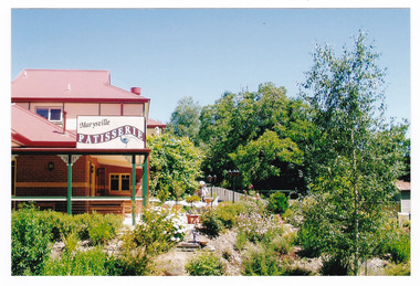 Shows the front corner of the building of the Marysville Patisserie in Marysville in Victoria. Shows a corner of the front garden next to the building.