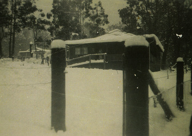 Shows a snow covered fenced landscape with a house in the background.
