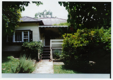 Shows the front facade of Past Favorites in Marysville in Victoria. Shows a weatherboard house with stairs leading up to the front verandah. The building is surrounded by trees.