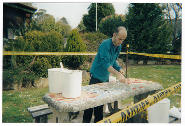 Shows a man decorating a wooden table outside a the Marysville Visitor Information Centre in Victoria.